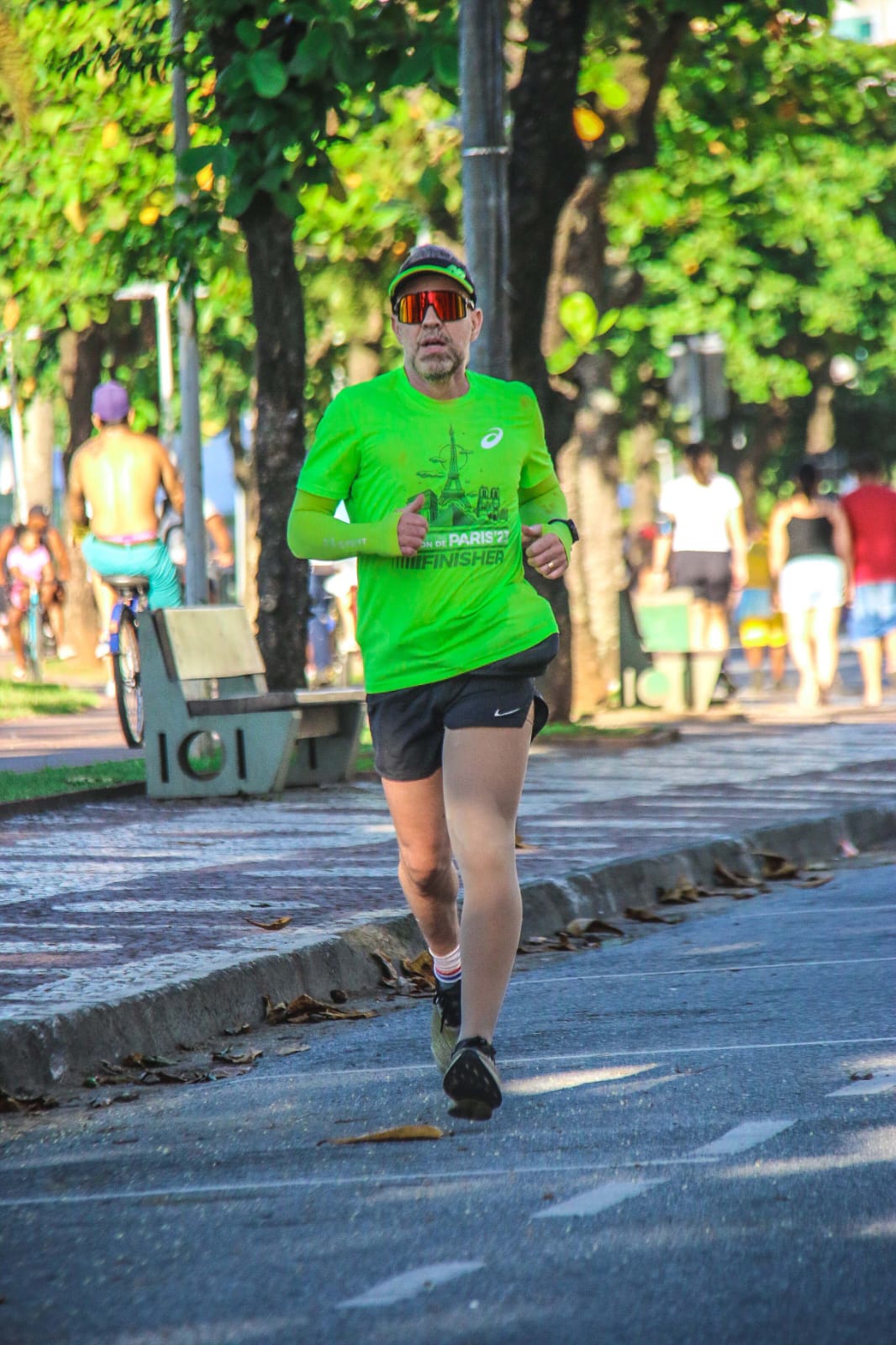 César Aarão correndo ao ar livre com camiseta verde e boné amarelo
